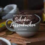 Man sieht einen Holztisch, darauf steht in der Mitte eine große Tasse mit einem Schoko-Tassenkuchen.