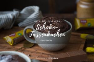 Man sieht einen Holztisch, darauf steht in der Mitte eine große Tasse mit einem Schoko-Tassenkuchen.