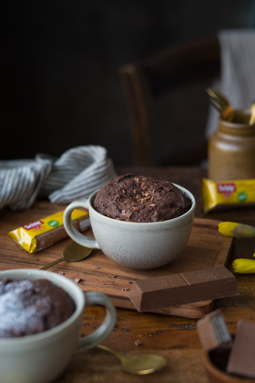 Man sieht einen Holztisch, darauf steht in der Mitte eine große Tasse mit einem Schoko-Tassenkuchen.