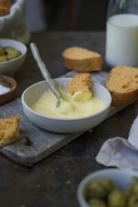 Aioli ohne Ei in einer kleinen Schale aus Porzellan mit Brot zum Dippen auf einem dunklen Hintergrund