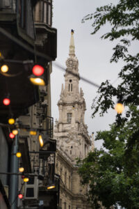 Ein spitzer Kirchturm im Hintergrund und bunte Lichterketten im Vordergrund, Budapest, Straßenszene