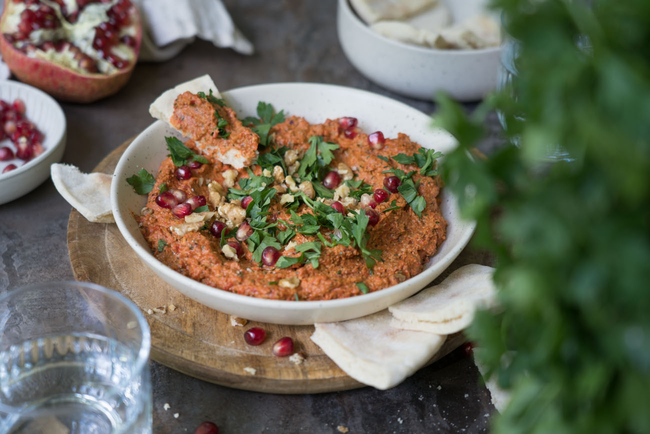 Muhammara in einer hellen Keramikschale, Petersilie im Vordergrund (unscharf), Pitabrot zum dippen