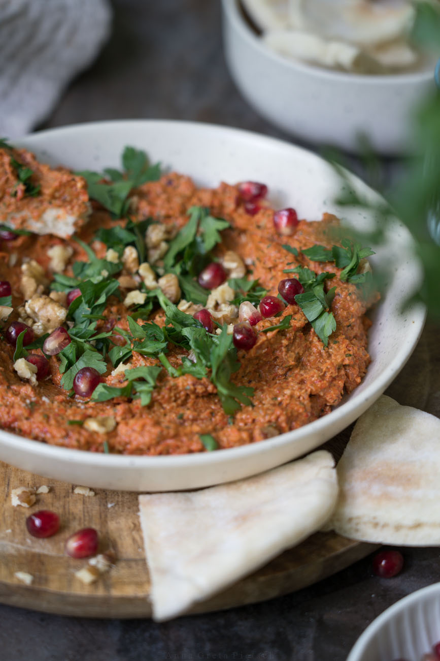 Muhammara in einer kleinen Keramik-Schale. Geschnittene, glatte Petersilie und Granatapfelkerne sind darauf gestreut.