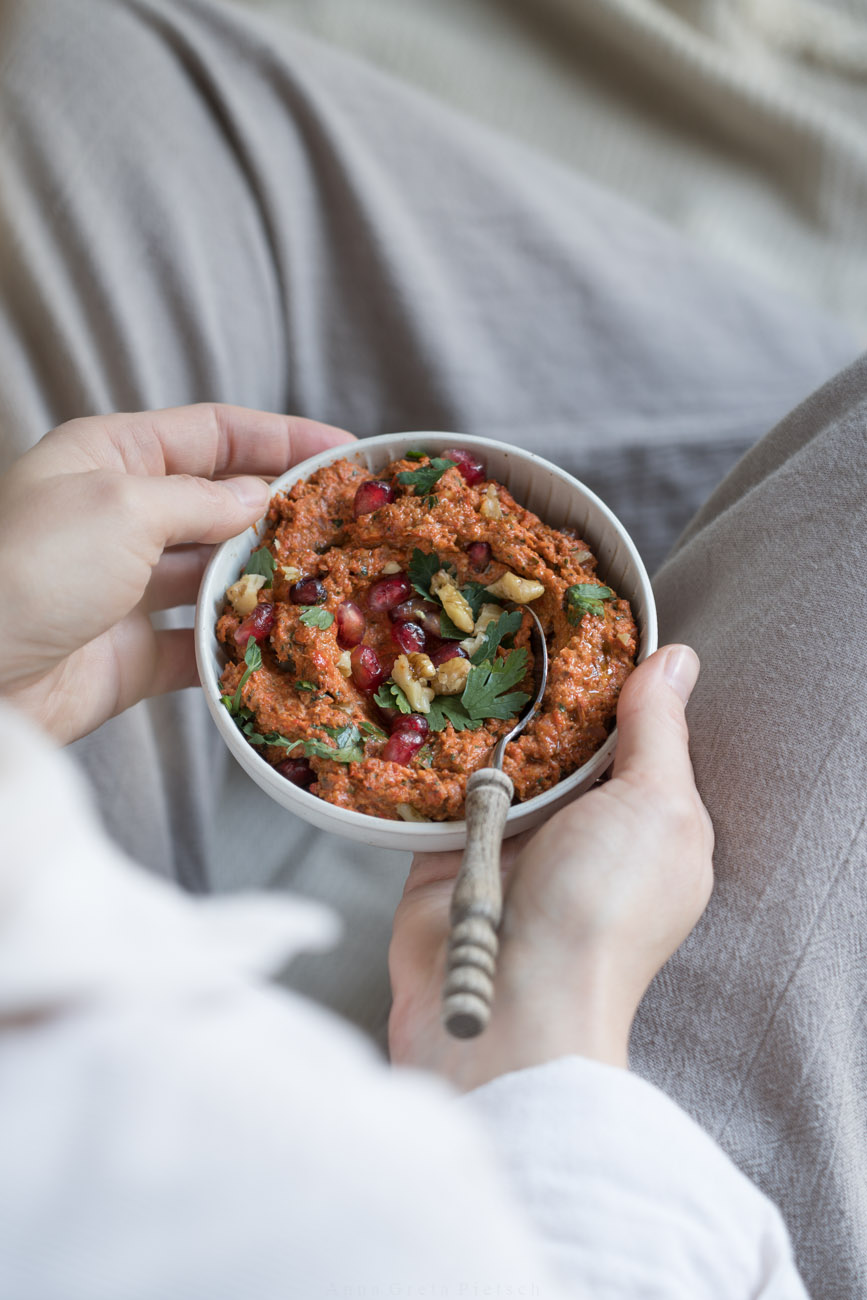 Muhammara in einer kleinen Keramik-Schale. Geschnittene, glatte Petersilie und Granatapfelkerne sind darauf gestreut.
