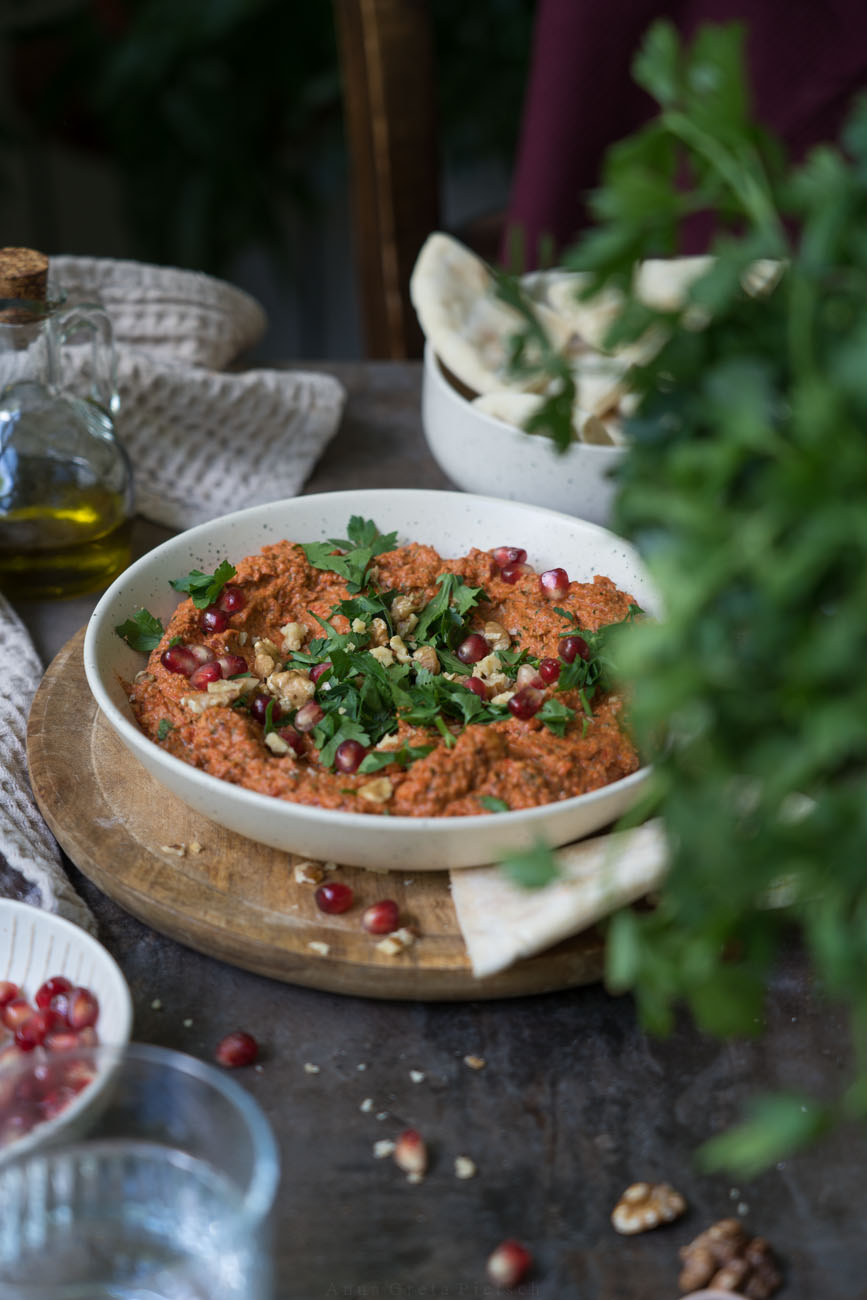 Muhammara in einer hellen Keramikschale, Petersilie im Vordergrund (unscharf), Pitabrot zum dippen