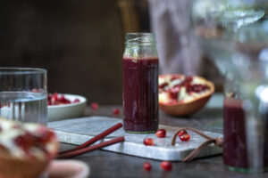 Selbstgemachter Granatapfelsirup in einer kleinen Glasflasche, steht auf einem kleinen Tablett aus Marmor