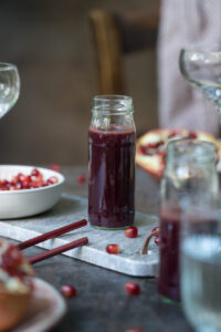 Selbstgemachter Granatapfelsirup in einer kleinen Glasflasche, steht auf einem kleinen Tablett aus Marmor