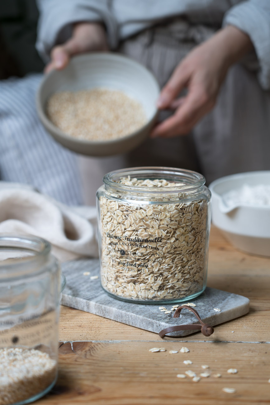 Ein Vorratsglas mit Haferflocken gefüllt, im Hintergrund wird eine Schale mit Amaranth-Pops gehalten.