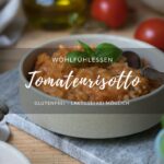 Titelbild für ein Rezept für Tomatenrisotto: Tomatenrisotto in einer beigen Schale auf einem Marmorbrettchen. ImHintergrund sieht man frische Tomaten und im Vordergrung etwas unscharf Basilikum.