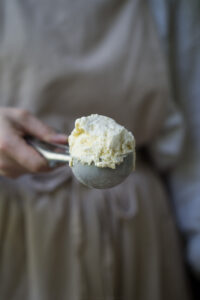 Eine Kugel Vanilleeis in einem Eisportionierer, gehalten von einer Hand