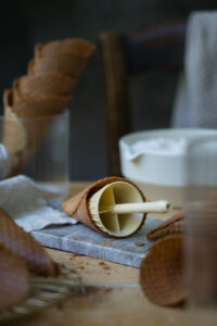 Zubereitung von Waffelhörnchen, man sieht eine selbstgemachte Eiswaffel, die auf einen Kegel aufgewickelt ist