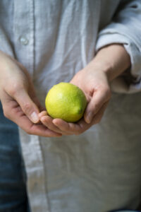 Eine frische Zitrone mit Wassertropfen wird von zwei Händen gehalten.