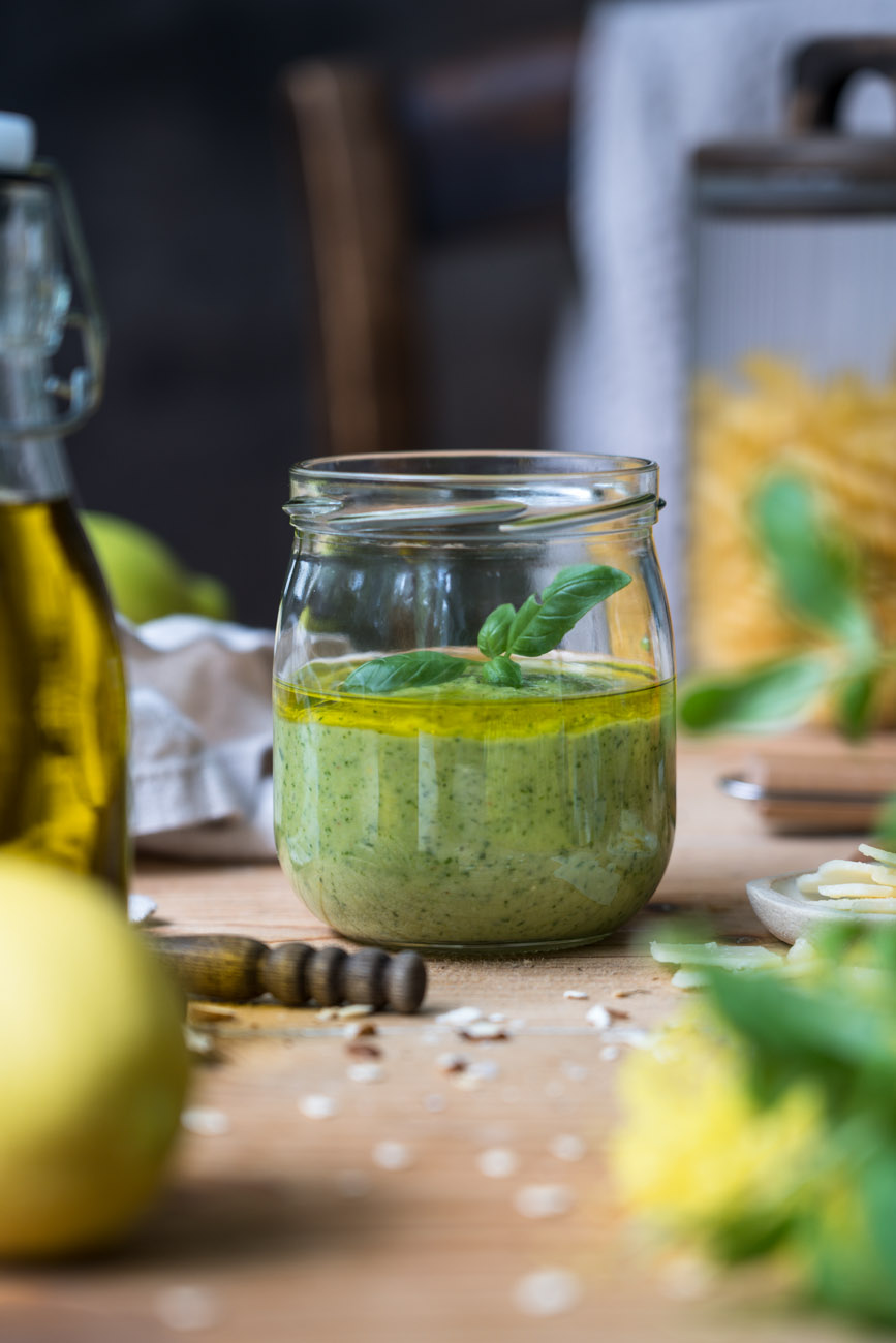 Ein Schraubglas mit Zitronen-Pesto, im Hintergrund steht ein Vorratsglas mit Pasta, vorne erkennt man eine Zitrone und eine Ölflasche am Rand.