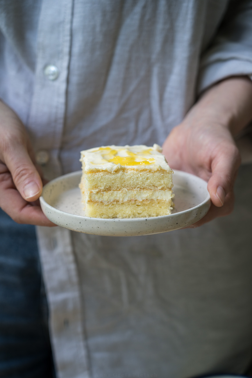 Ein kleiner Teller mit einem Stück Zitronen-Tiramisu wird von zwei Händen gehalten.