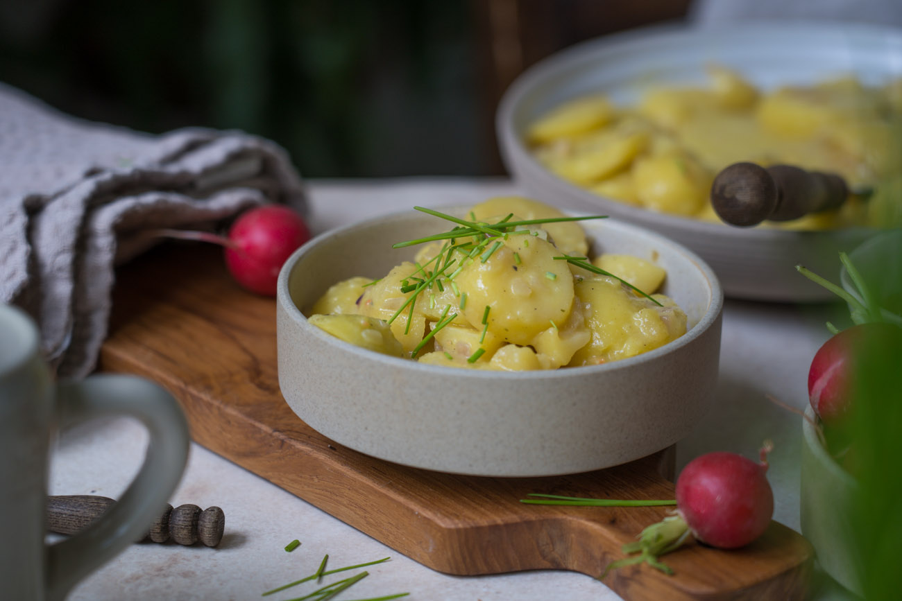 Ein gedeckter Tisch. In der Mitte steht eine Schale mit bayerischem Kartoffelsalat, rundherum stehen Radieschen, ein Bierkrug.