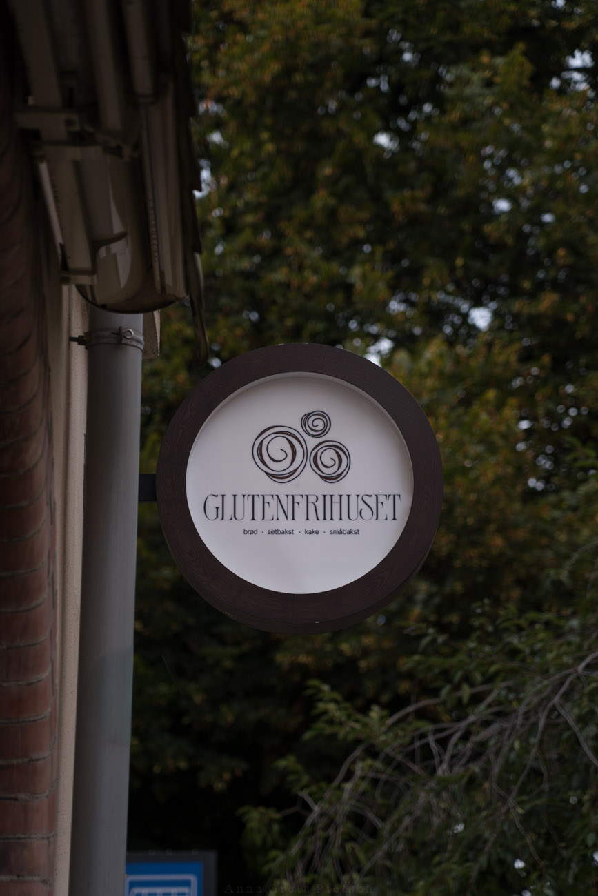 Ein rundes Schild an einer Hausfassade mit der Aufschrift "Glutenfihuset", eine glutenfreie Bäckerei/Café in Oslo, Norwegen.