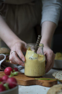 Ein Einmachglas mit selbstgemachter Burgersoße mit süßem Send, auf einem gedeckten Tisch/einer Anrichte, gehalten von zwei Händen.
