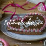 Ein Holztisch mit einem hellen Keramikteller, auf dem ein Lebkuchenherz mit der Aufschrift "Mausi" liegt.