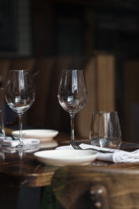 Ein Blick in ein Restaurant auf einen eingedeckten Tisch mit weißen Servierten und Gläsern.