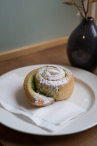 Eine Zimtschnecke auf einem weißen Teller, mit Puderzucker bestreut, "Glutenfihuset", eine glutenfreie Bäckerei/Café in Oslo, Norwegen.
