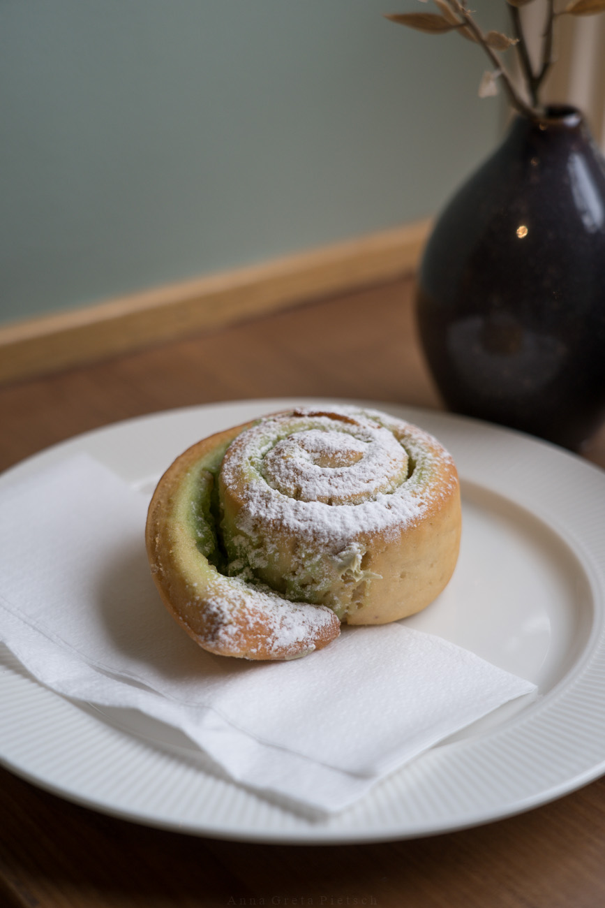 Eine Zimtschnecke auf einem weißen Teller, mit Puderzucker bestreut, "Glutenfihuset", eine glutenfreie Bäckerei/Café in Oslo, Norwegen. 