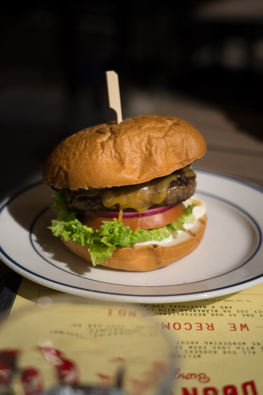 Ei weißer Teller mit einem Burger, belegt mit einem Pattie aus Fleisch, Tomate, Salat und Zwiebel.