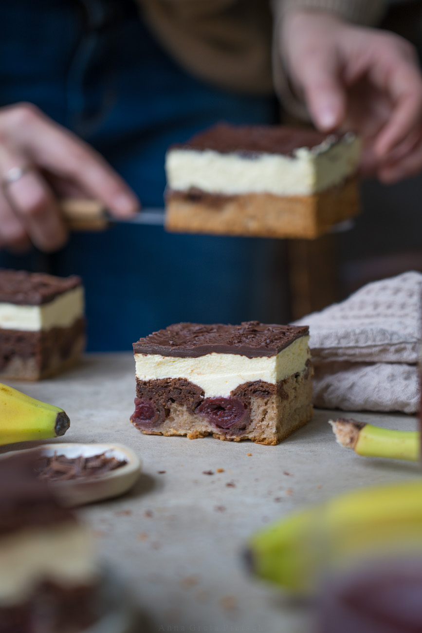 Ein Stückchen Kuchen liegt auf einer hellen Platte, weiter sieht man Banane und weitere Kuchenstücke. Es ist eine Donauwelle mit einem Boden aus Bananenbrot.