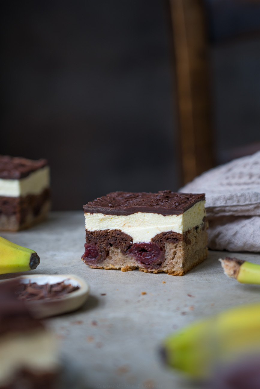 Ein Stückchen Kuchen liegt auf einer hellen Platte, weiter sieht man Banane und weitere Kuchenstücke. Es ist eine Donauwelle mit einem Boden aus Bananenbrot.
