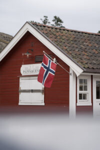 Ein rotes Holzhaus mit weißen Fensterrahmen und Tür in Oslo. Außen ist eine norwegische Flagge angebracht.