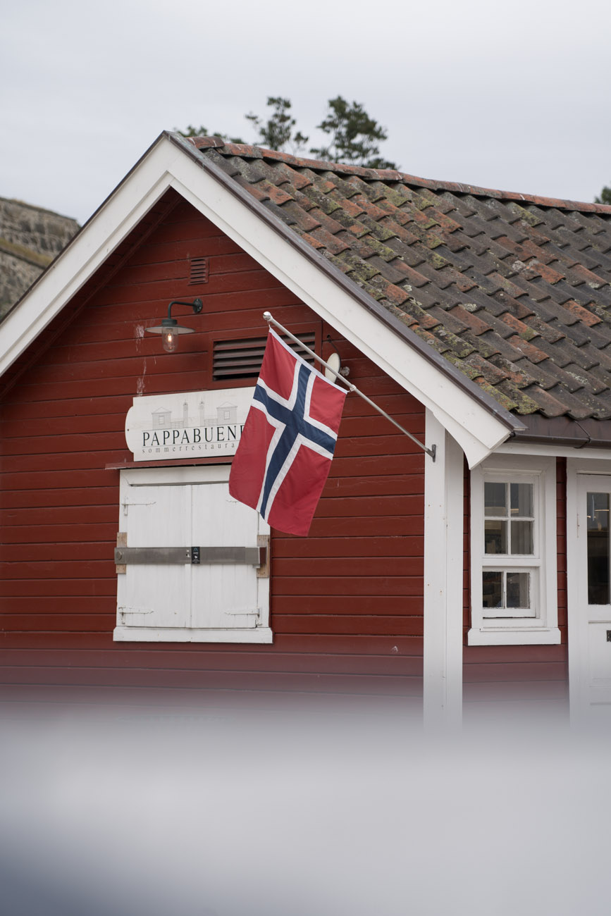 Ein rotes Holzhaus mit weißen Fensterrahmen und Tür in Oslo. Außen ist eine norwegische Flagge angebracht.