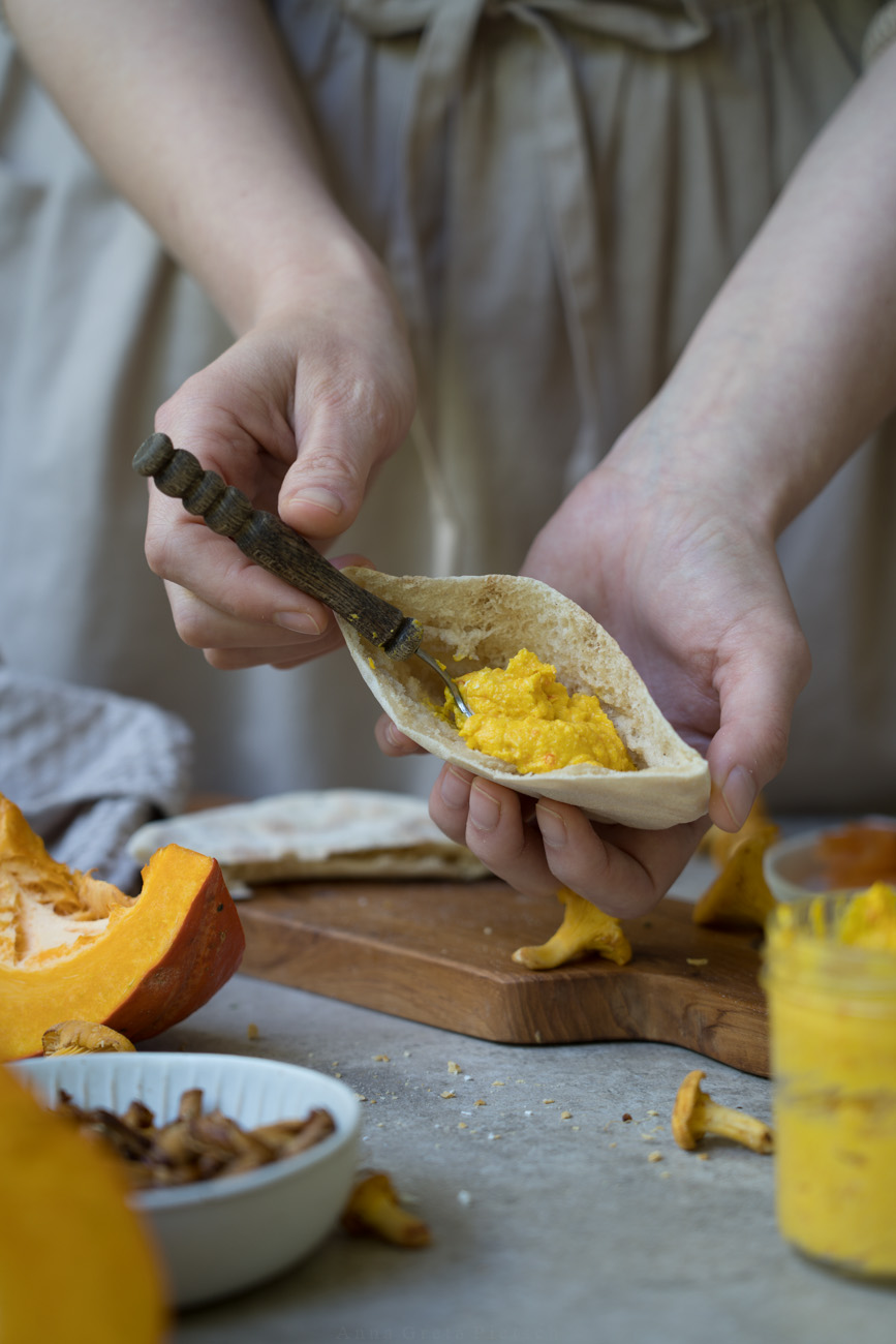 Eine aufgetrennte Pitatasche wird mit einer orangenen Creme aus Kürbis und Feta gefüllt.