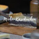 Titelbild für einen Blogbeitrag/Rezept für Mohn-Käsekuchen. Ein Stück Mohn-Käsekuchen auf einem Holzbrett, im Hintergrund sieht man einen Teller mit Kuchen. Dazu stehen Gläser mit Tee auf dem Tisch.