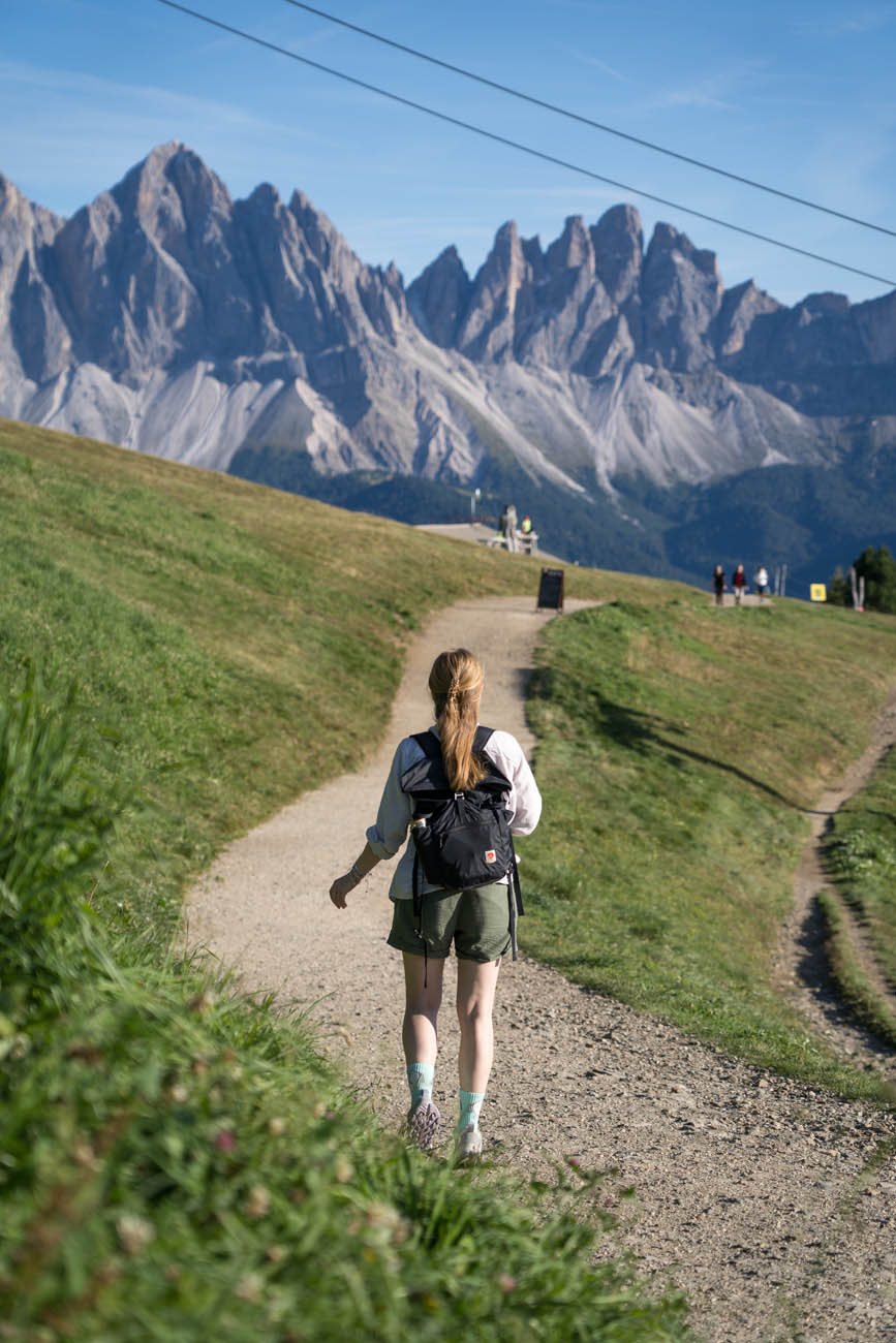 Eine Person mit Wanderrucksack auf einem Wanderweg, im Hintergrund sieht man die Dolomiten.