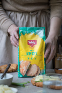 Eine Packung glutenfreies Mehl für Brote, gehalten von zwei Händen auf einer Küchenarbeitsfläche. Die Packung ist gelb-türkis.