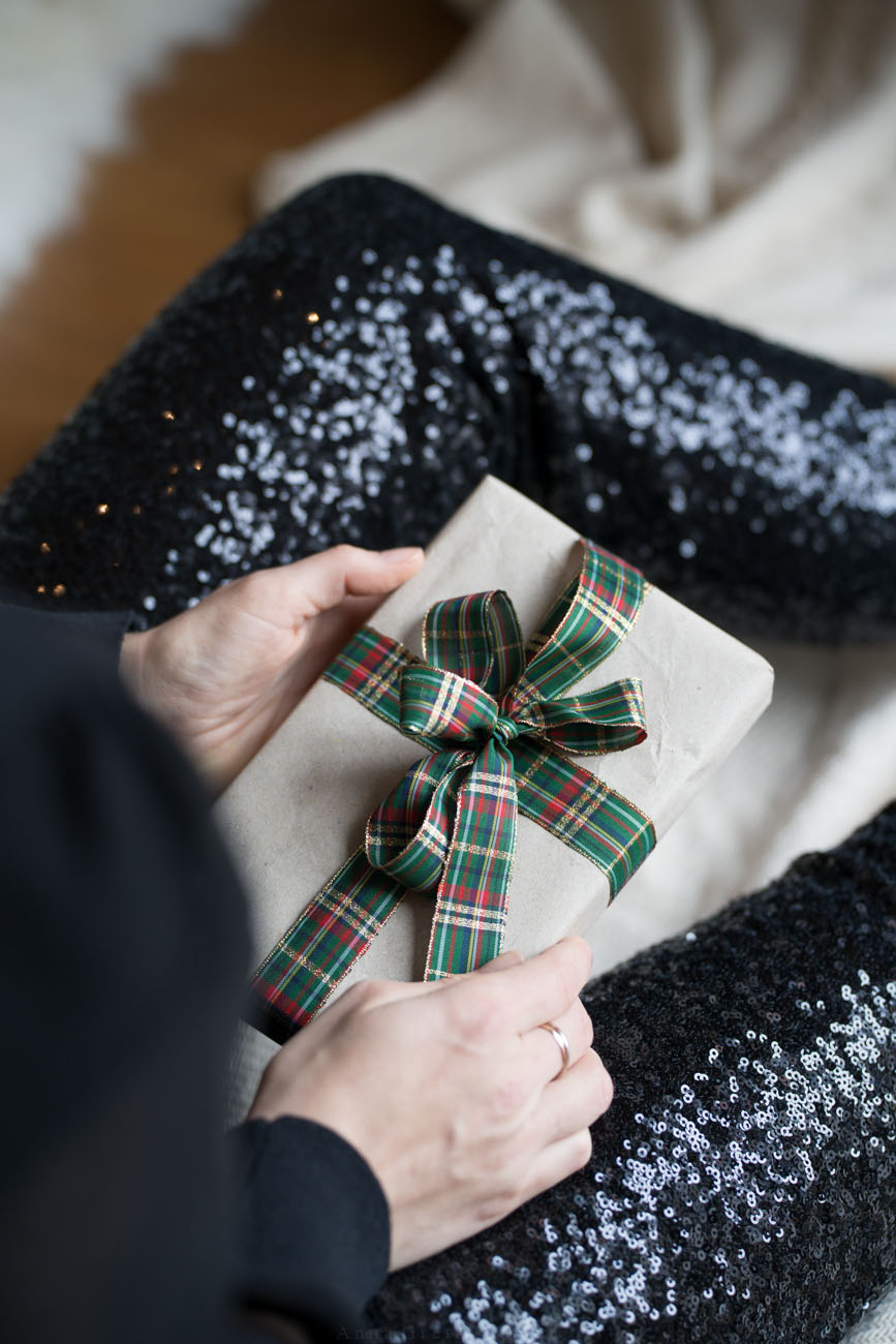 Eine Person sitzt in festlicher Kleidung (Pailetten-Hose) auf eier Decke auf dem Boden und hält ein Geschenk in den Händen.