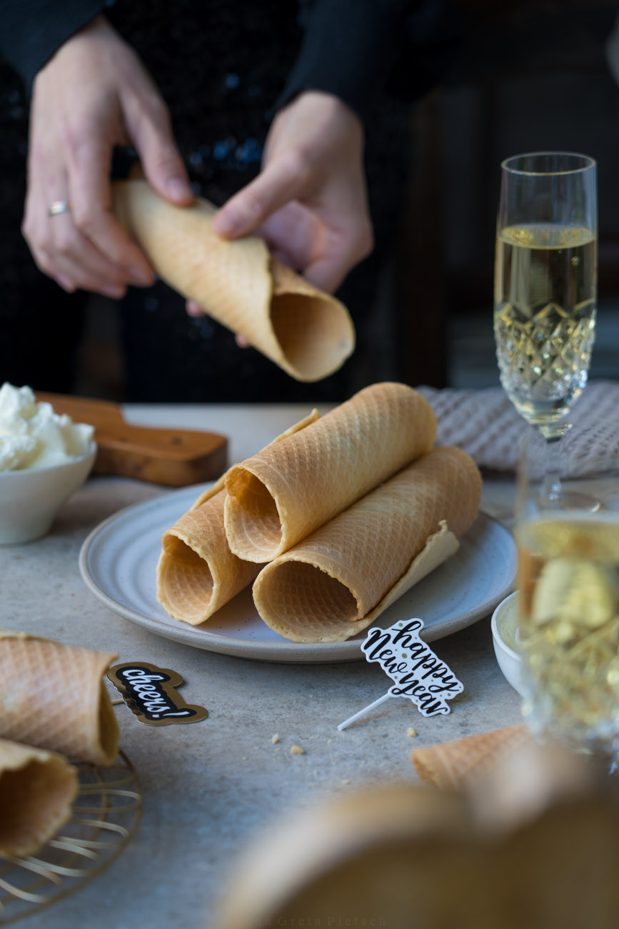 Ein Tisch gedeckt mit Sektgläsern, in der Mitte steht ein Teller mit gerollten, knusprigen Waffeln.