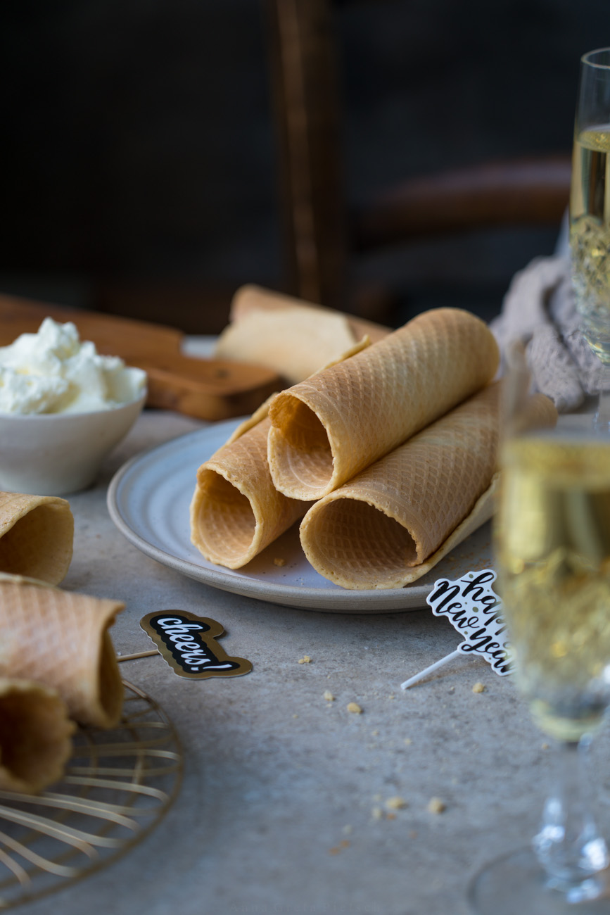 Ein Tisch gedeckt mit Sektgläsern, in der Mitte steht ein Teller mit gerollten, knusprigen Waffeln.