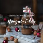 Ein kleines Fläschchen mit Nougat-Likör steht auf einem Marmorbrettchen. An der Flasche ist eine Schleife und der Tisch ist ein wenig weihnachtlich dekoriert.