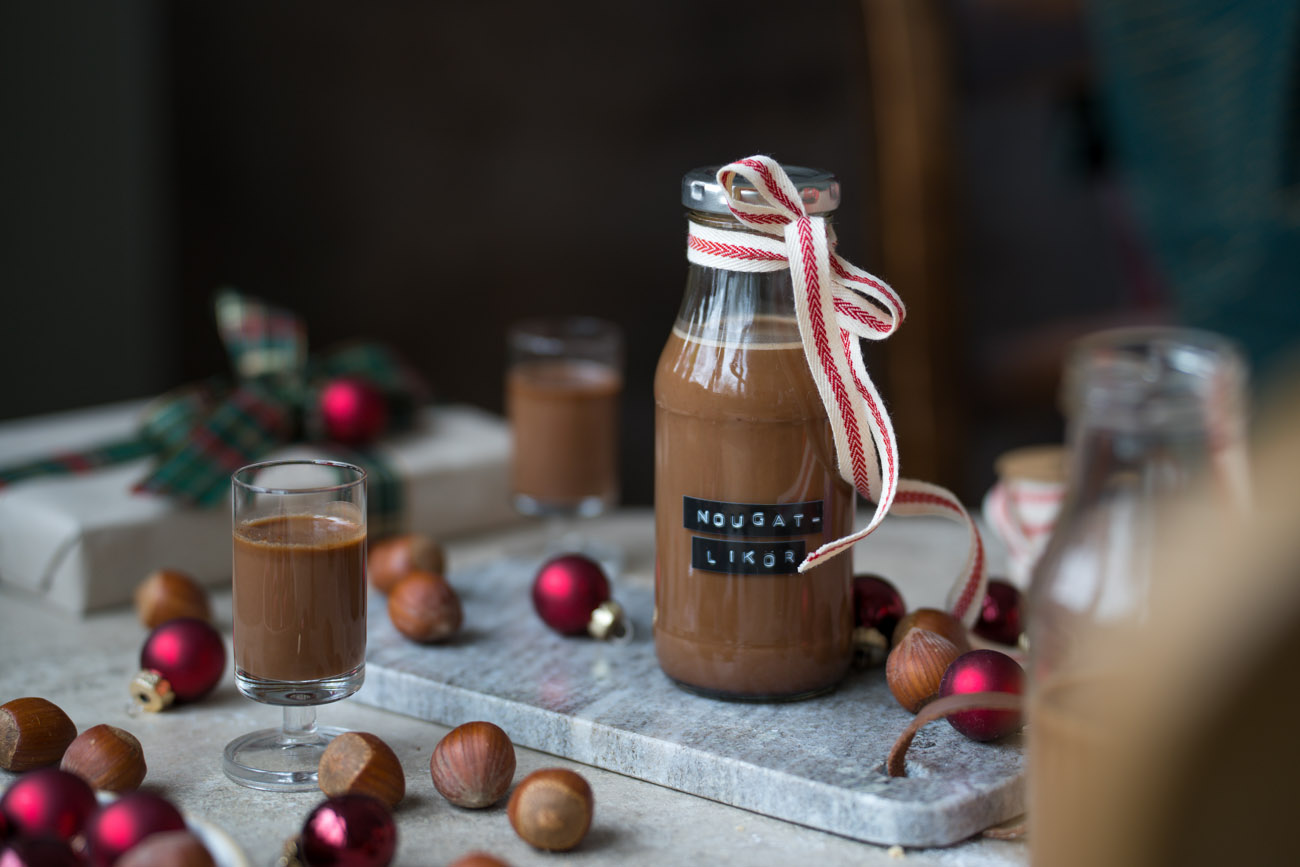 Ein kleines Fläschchen mit Nougat-Likör steht auf einem Marmorbrettchen. An der Flasche ist eine Schleife und der Tisch ist ein wenig weihnachtlich dekoriert.