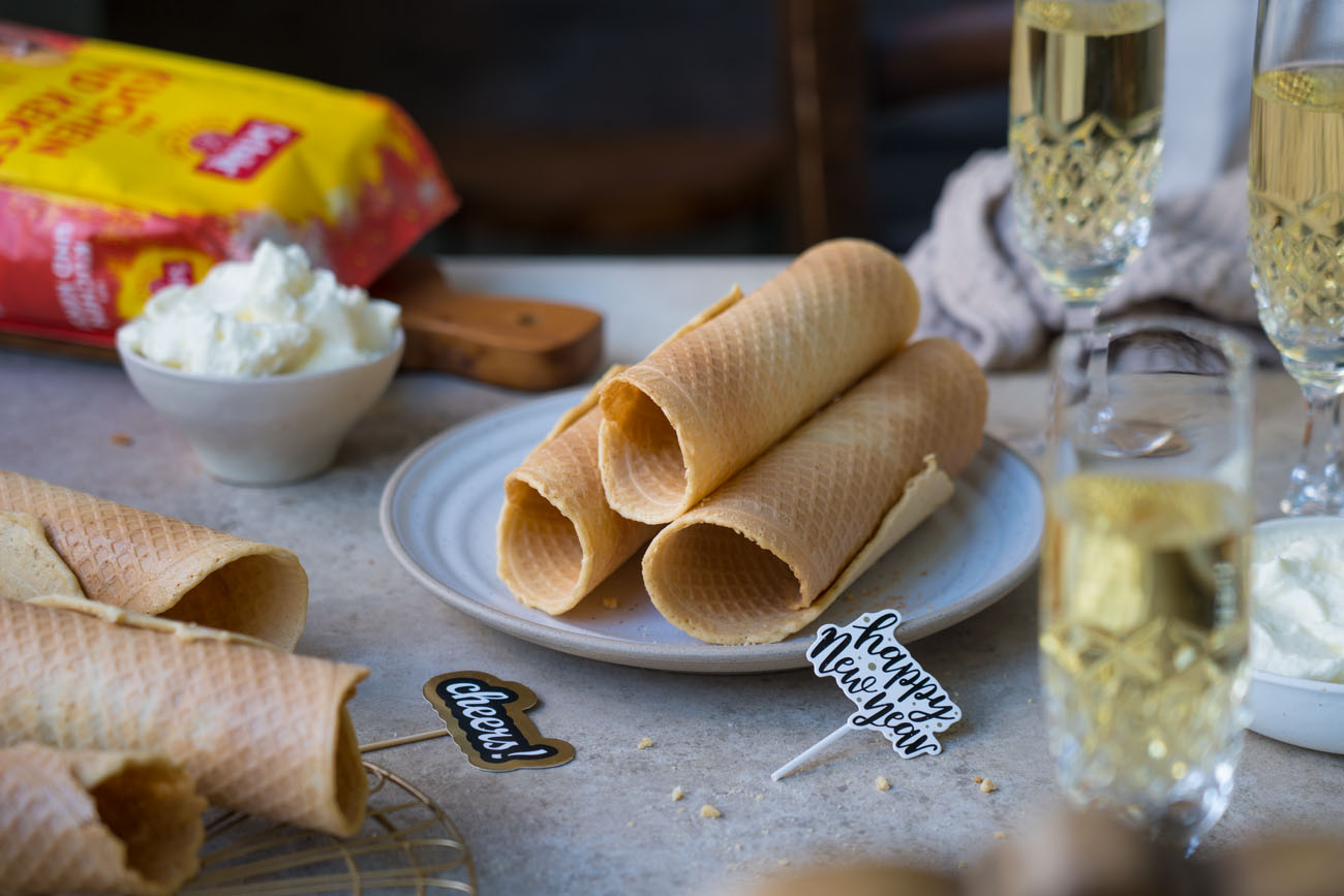 Ein Tisch gedeckt mit Sektgläsern, in der Mitte steht ein Teller mit gerollten, knusprigen Waffeln.