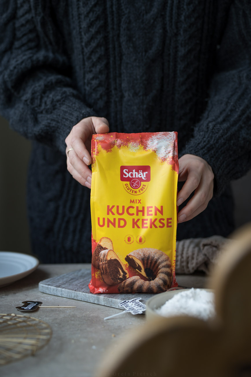 Eine Arbeitsfläche, in der Mitte wird ein Paket mit glutenfreiem Mehl von zwei Händen gehalten.