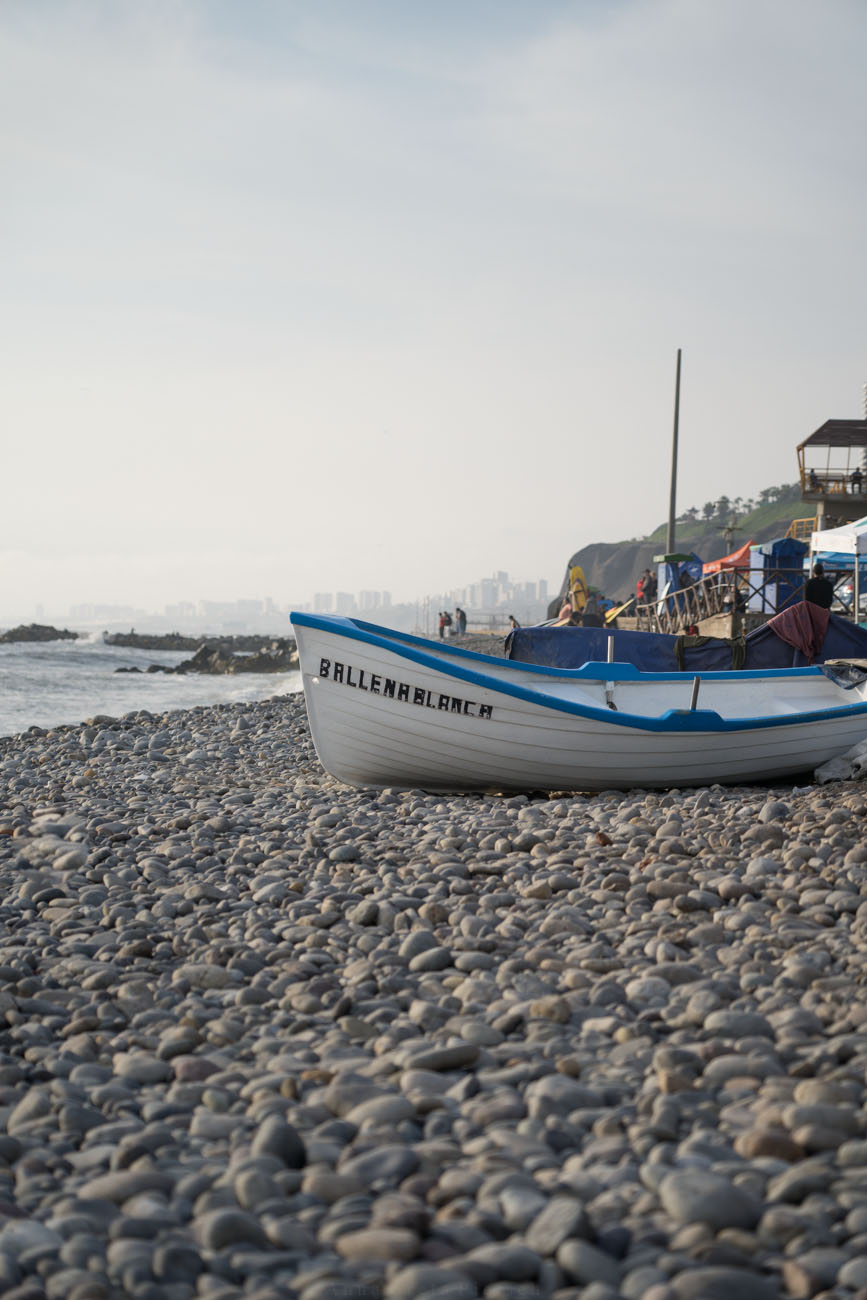 Ein weißes Holzboot mit einem blauen Rand liegt an einem Kieselstrand, Lima, Peru.