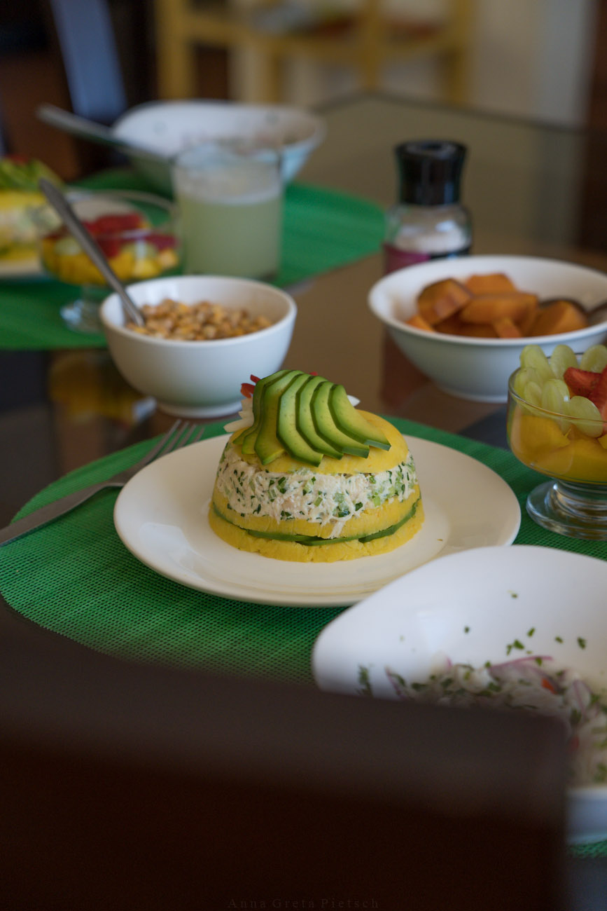 Ein gedeckter Tisch nach einem Kochkurs in Peru. Man sieht das Gericht Causa auf einem Teller, ein Gericht aus Kartoffeln und einer Thunfischcreme, Ceviche, Obstsalat und ein Schälchen mit gerösteten Maiskörnern.