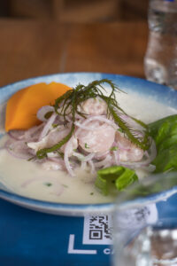 Ein Holztisch mit einem Teller. Darauf ist frisch zubereitetes Ceviche mit gekochter Süßkartoffel als Beilage.
