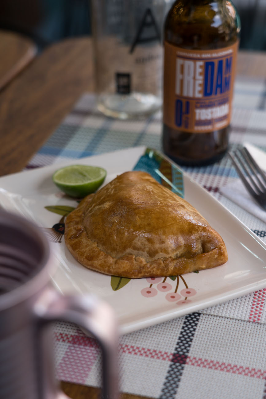 Ein gedeckter Holztisch mit einer glutenfreien Empanada auf einem Teller in der Mitte.