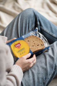 Eine PErson sitzt auf einer Decke im Wohnzimmer und hält eine Packung mit glutenfreiem Landbrot in ihren Händen.