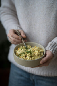 Eine Person hält eine Keramikschüssel in beiden Händen. Darin ist veganer Eiersalat.