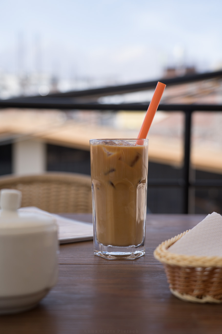 Ein Eiskaffee in einem großen Glas auf einem Tisch. Im Glas steckt ein orangefarbener, dicker Strohhalm.