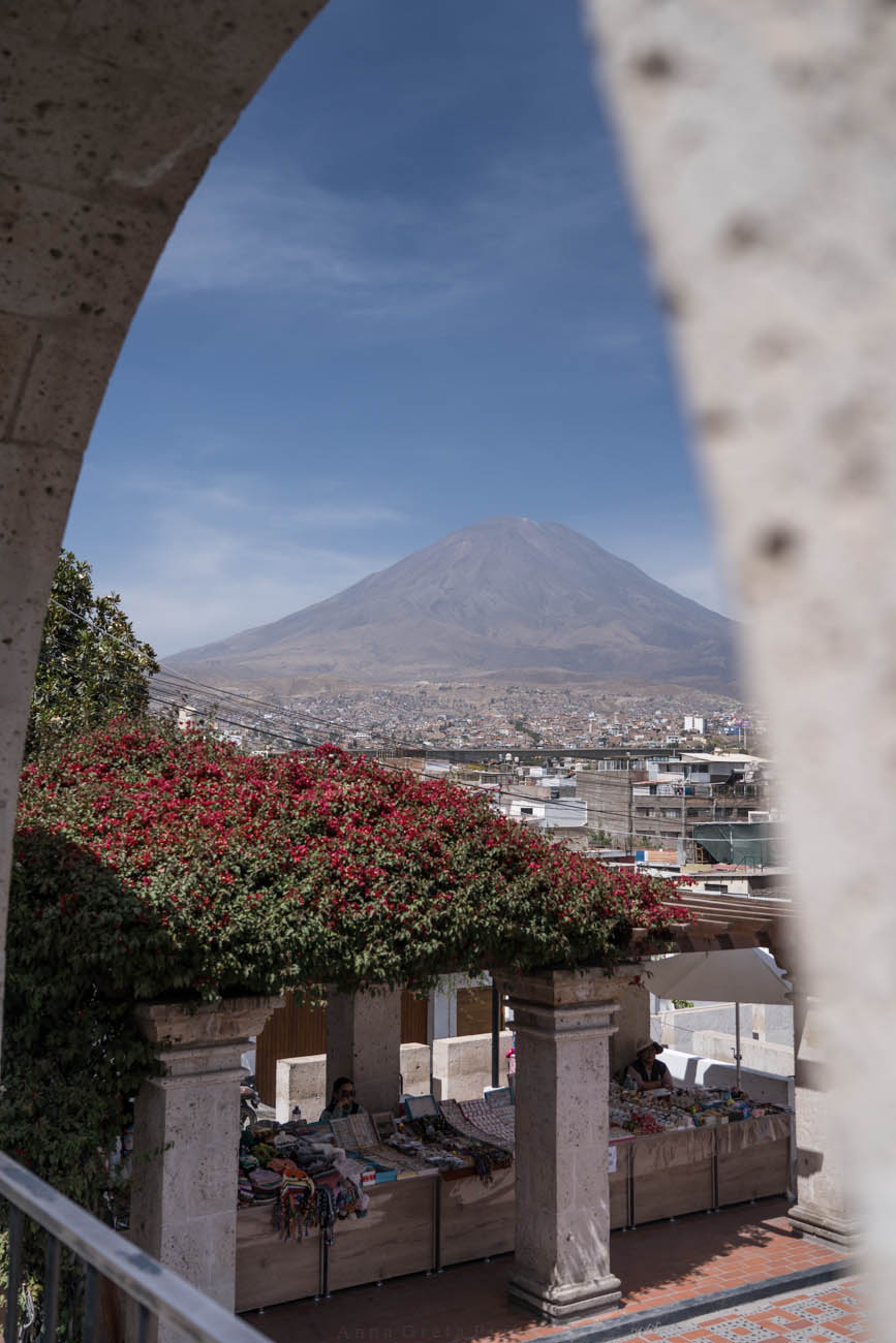 Man sieht den berühmten Mirador de Yanahuara in Arequipa, einen bekannten Aussichtspunkt. Durch Torbögen kann man die Vulkane in der Entfernung sehen.
