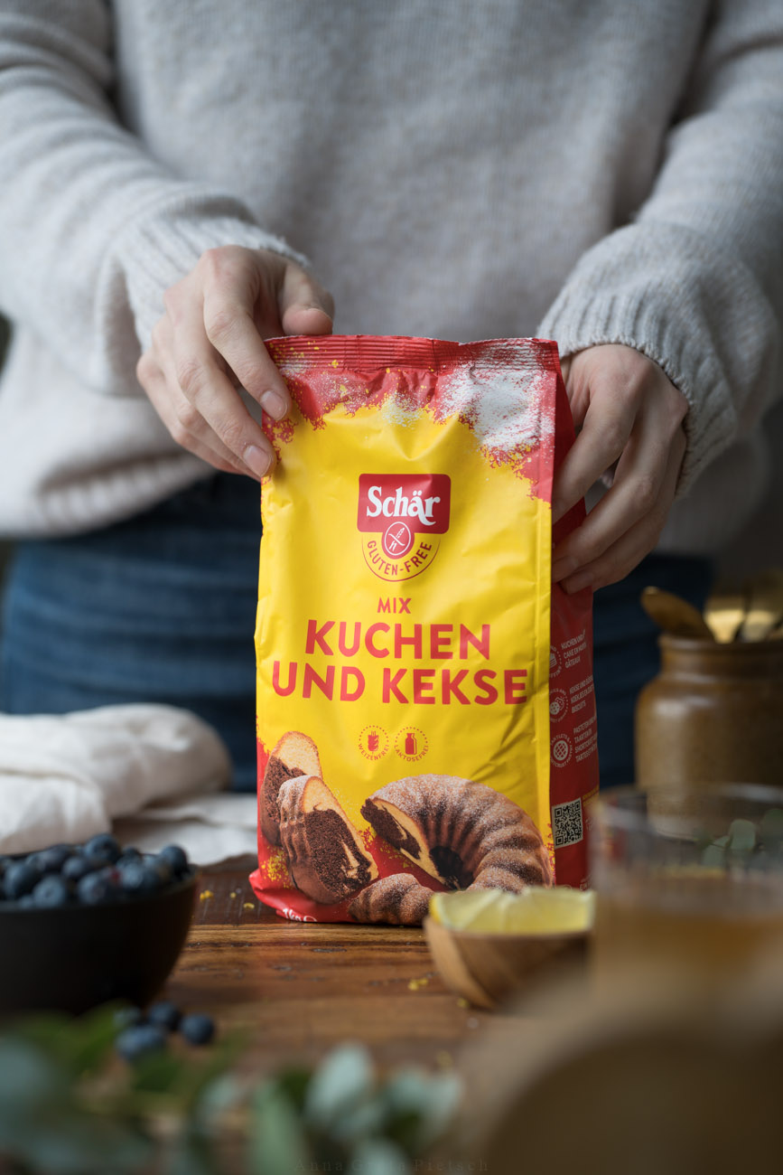Eine Arbeitsfläche, in der Mitte wird ein Paket mit glutenfreiem Mehl von zwei Händen gehalten.